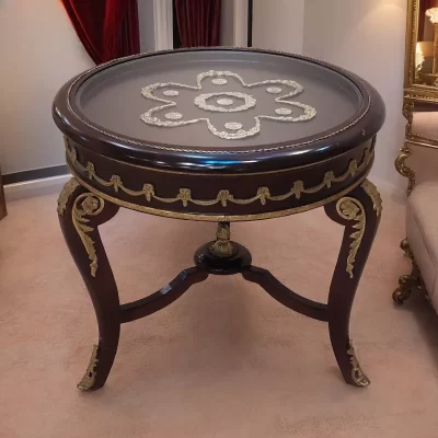ترابيزة جانبية دائرية مصنوعة من خشب الزان مع زخارف نحاسية وتصميم كلاسيكي فرنسي. سطح الطاولة مصنوع من الزجاج الشفاف.