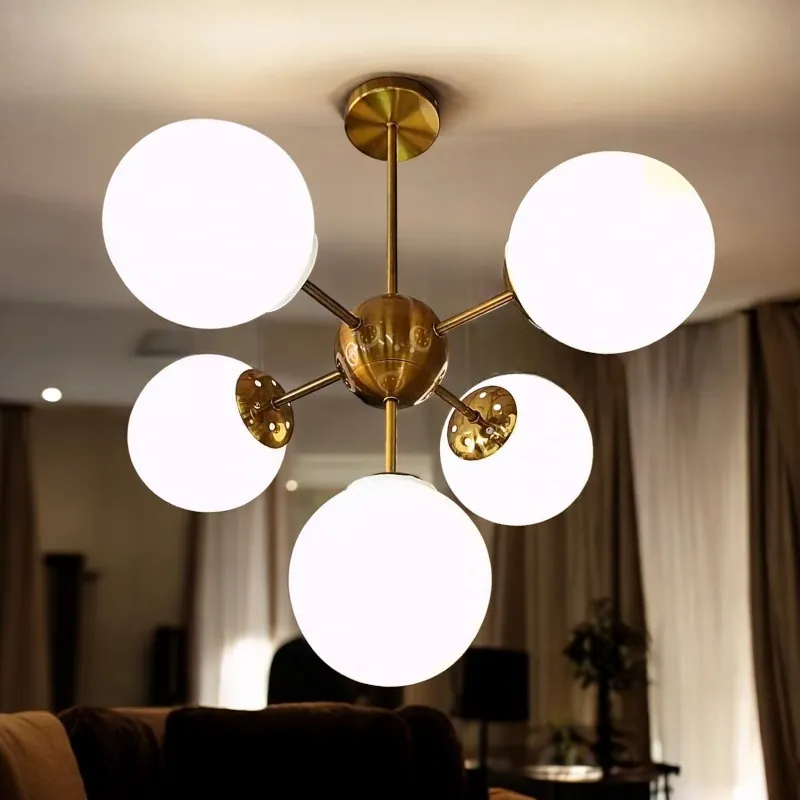 نجفة معدنية كلوبات كروية 5 ذراع بتصميم عصري موديل 028952 نجفة معدنية بطلاء نحاسى لامع وتصميم عصرى، مزودة بخمس كرات زجاجية بيضاء، وتبدو مضاءة فى غرفة المعيشة.