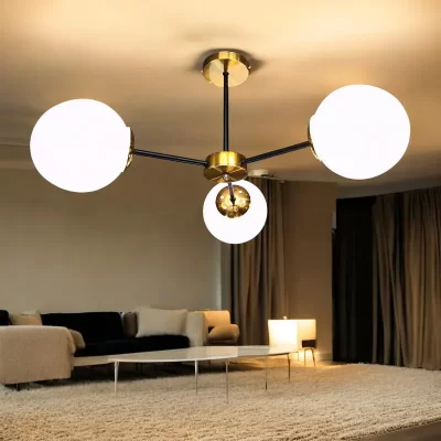 نجفة معاصرة بتصميم هندسي بسيط يتكون من ثلاثة أذرع سوداء تنطلق من قاعدة مركزية نحاسيةاللون، وينتهي كل ذراع بكرة زجاجية بيضاء مستديرة، وتبدو مضاءة داخل غرفة.