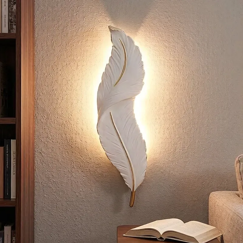إضاءة حائط LED عصرية بتصميم ريشة من الراتنج الأبيض والذهبي، مضاءة بنور دافئ لتزيين الجدران في غرف المعيشة.