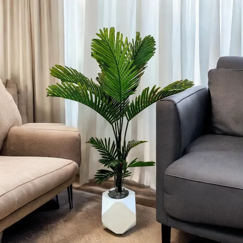نخلة قصب صناعية بأوراق خضراء طويلة وريشية، موضوع في إناء أبيض بتصميم هندسي. مثالي لتزيين أي مساحة داخلية في المنزل أو المكتب.